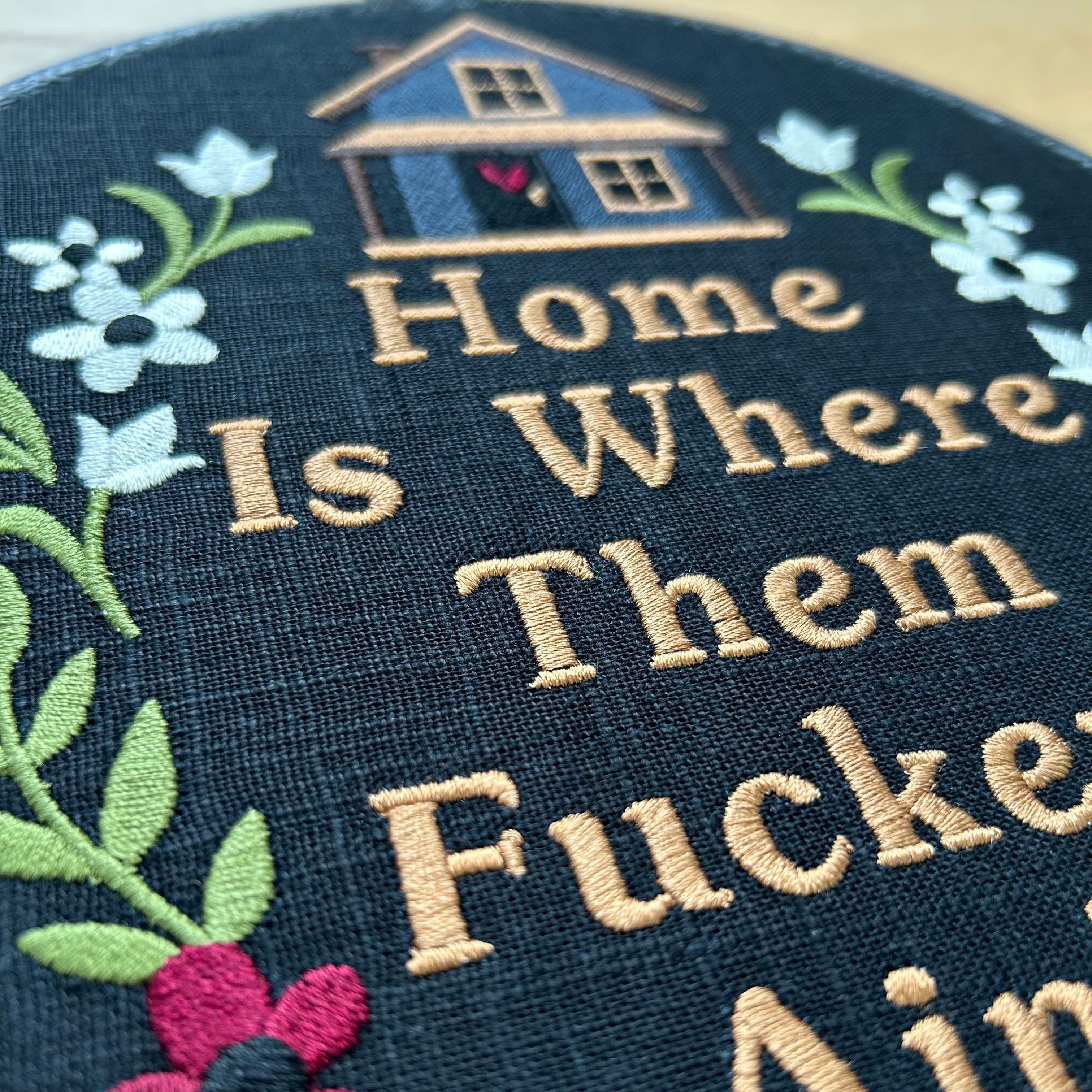 Black embroidered hoop art with a stitched house, flowers, and the funny quote ‘Home Is Where They Ain’t.’ Handmade humorous wall decor

