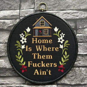 Funny embroidery hoop art saying ‘Home Is Where They Ain’t,’ surrounded by stitched flowers and a cozy house. Perfect for anyone who loves sarcastic or sassy handmade decor.
